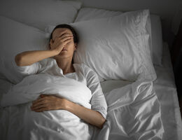 A woman tucked into bed with a hand over her face.