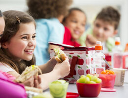 A smiling girl holds a sandwich in a school cafeteria.
