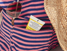 A sunscreen bottle peeks from a brightly striped bag, on which rest a hat and sunglasses.