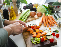Close-up of hands chopping vegetables on a cluttered kitchen counter.