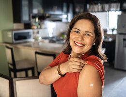 A smiling woman raises her sleeve to display her vaccine bandage.