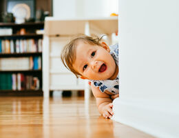 A baby peeks out from around a corner.