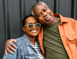 An older man smiles and side-hugs a young woman