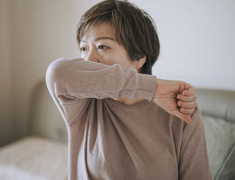 A woman coughs into her elbow.