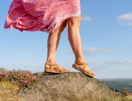 A lower-body view of a woman wearing sandals and standing on a rock.